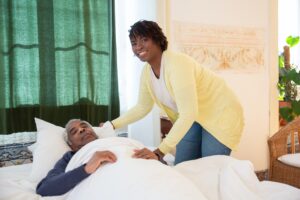 An elderly man being tucked into bed by care staff.