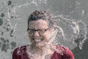 A woman winces as cold water is poured over her.,
